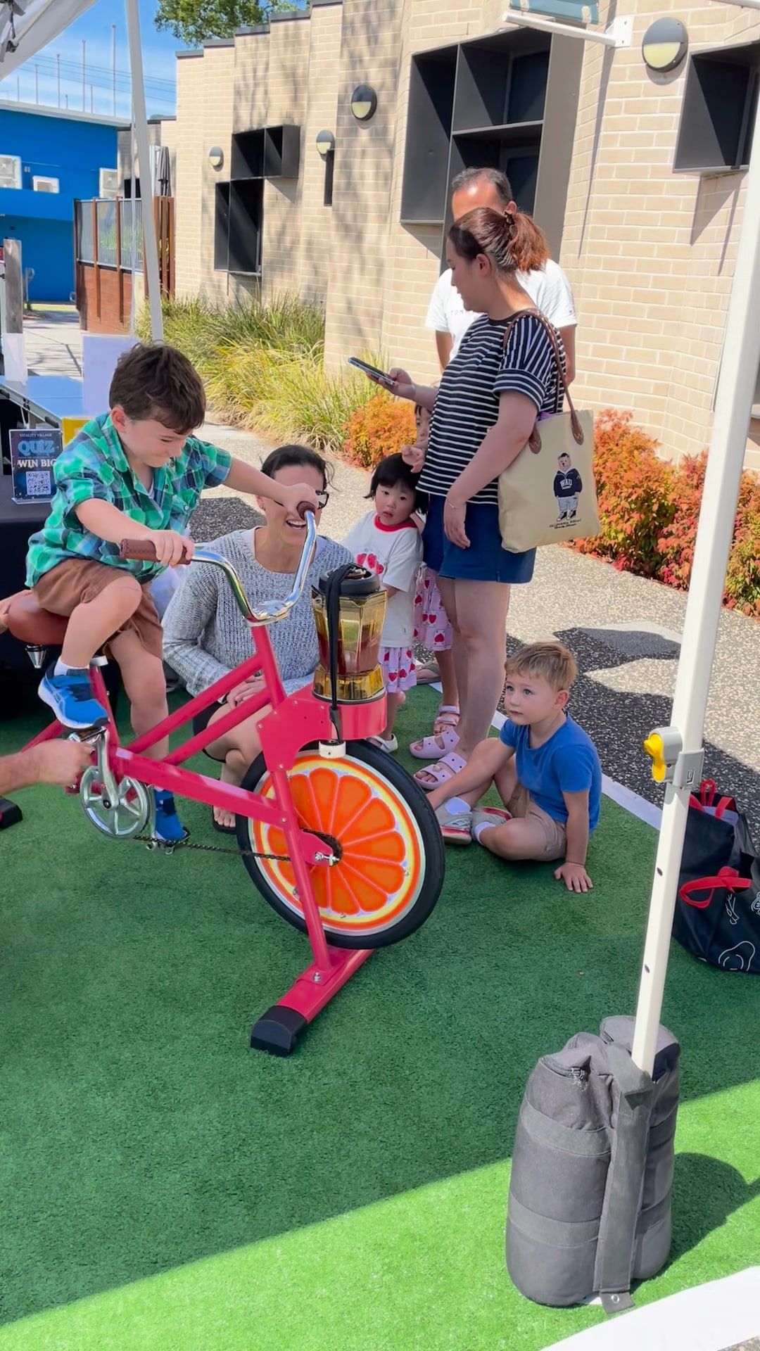 Children gather around the coral smoothie bike under the marquee