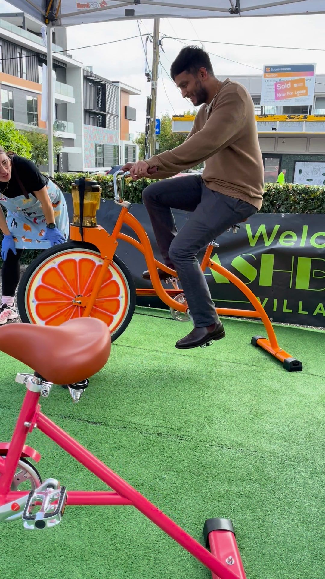 An adult pedals the coral smoothie bike at an outdoor event