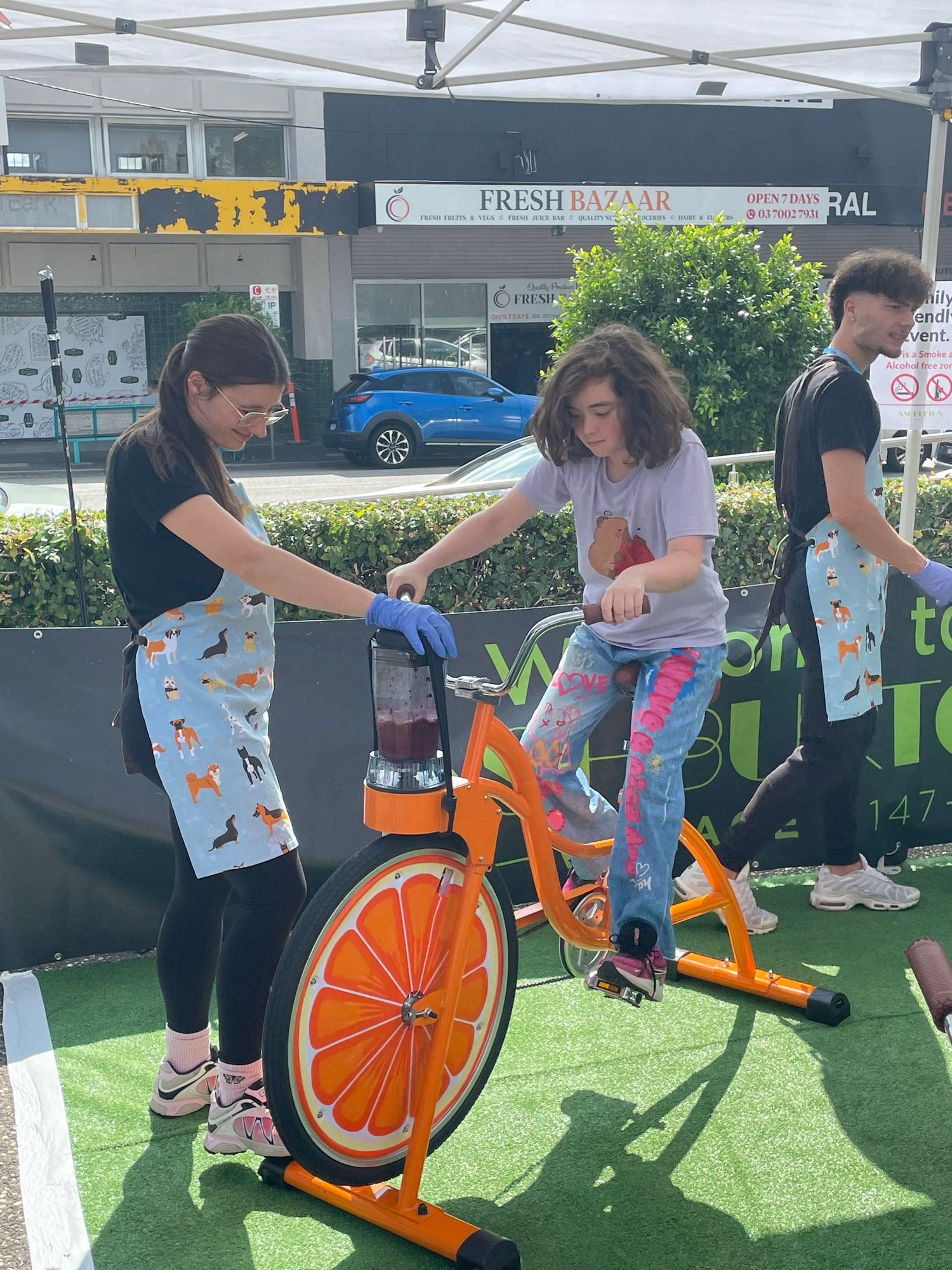 A child pedals the orange smoothie bike while a staff member steadies the jug